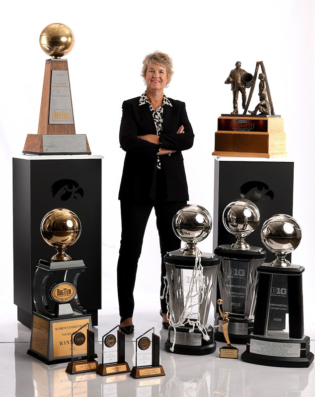Coach Bluder stands among the many trophies of the Iowa Women's Basketball team
