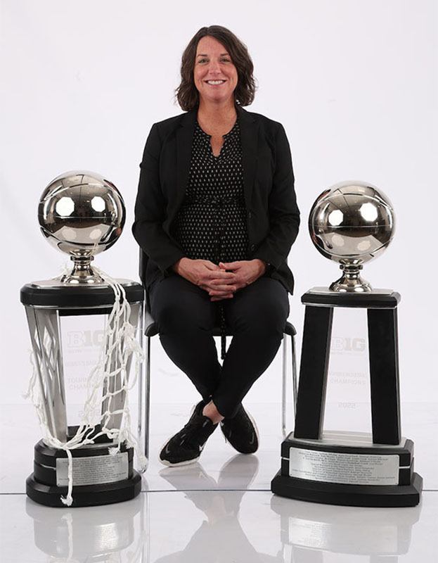 A woman seated with two basketball trophies on either side of her