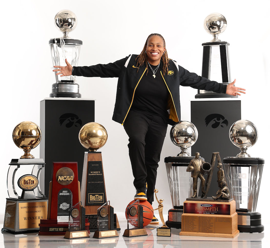 A woman stands, surrounded by basketball trophies