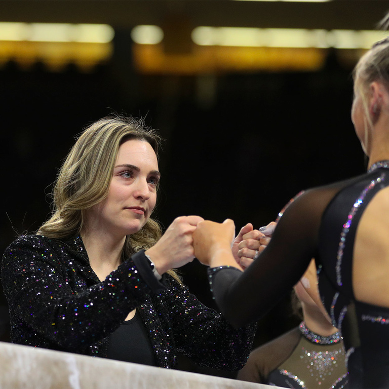 Assistant coach Jessa Hansen Parker fists bumps a female gymnast over the balance beam