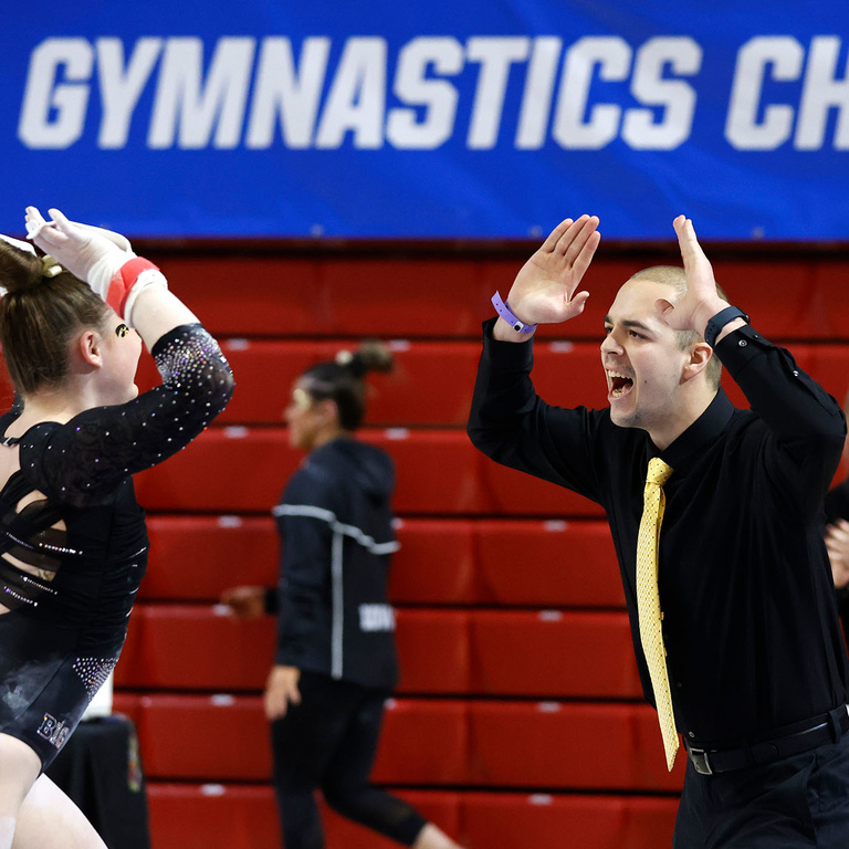 Assistant Coach Quest Hayden high fives a female gymnast