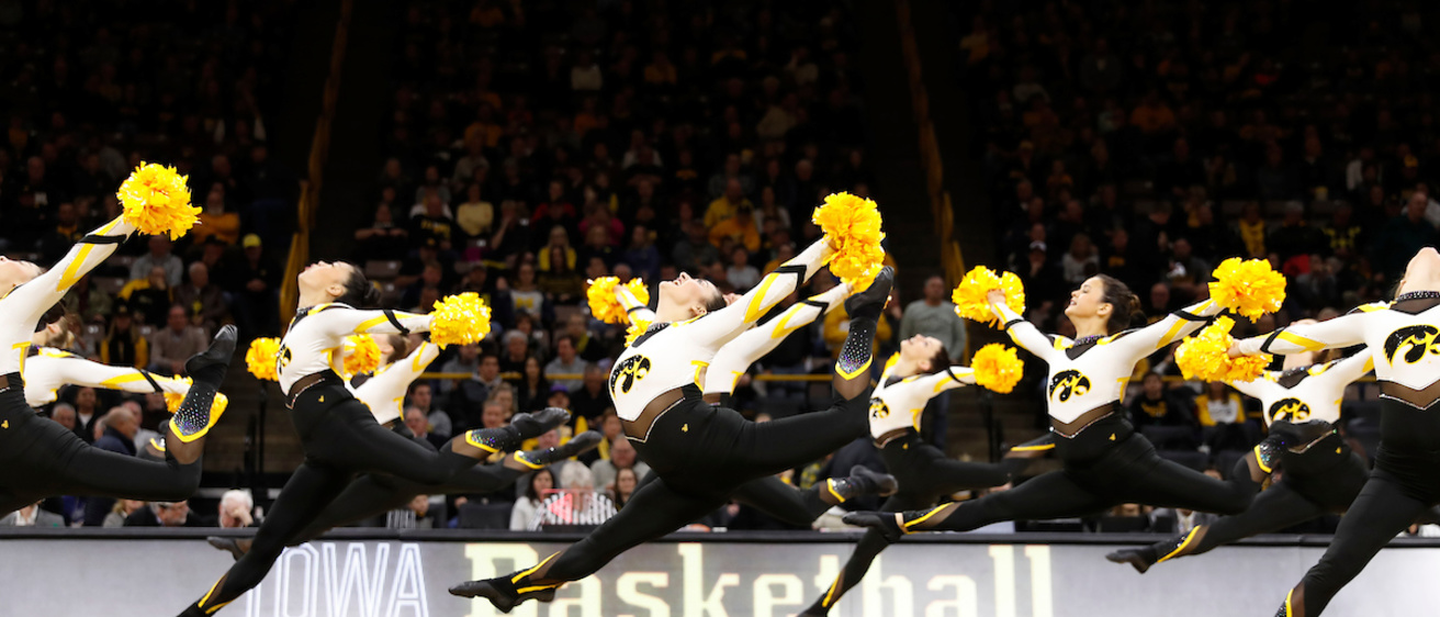A row of college spirit dancers leap across a basketball court