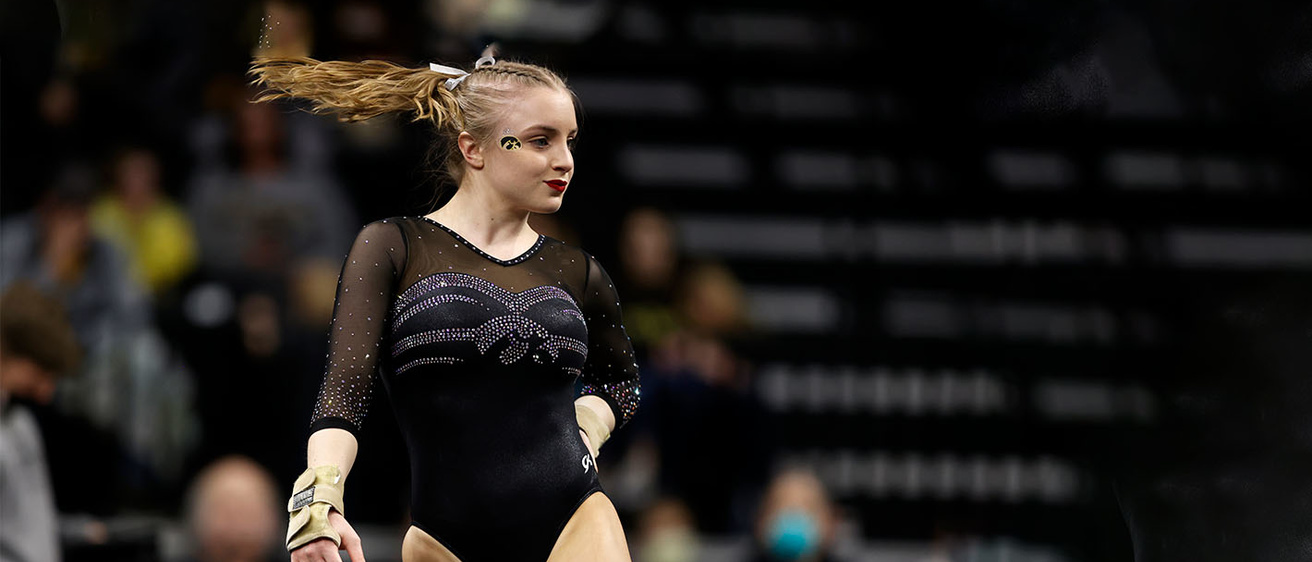 A gymnast in a black leotard stands and performs