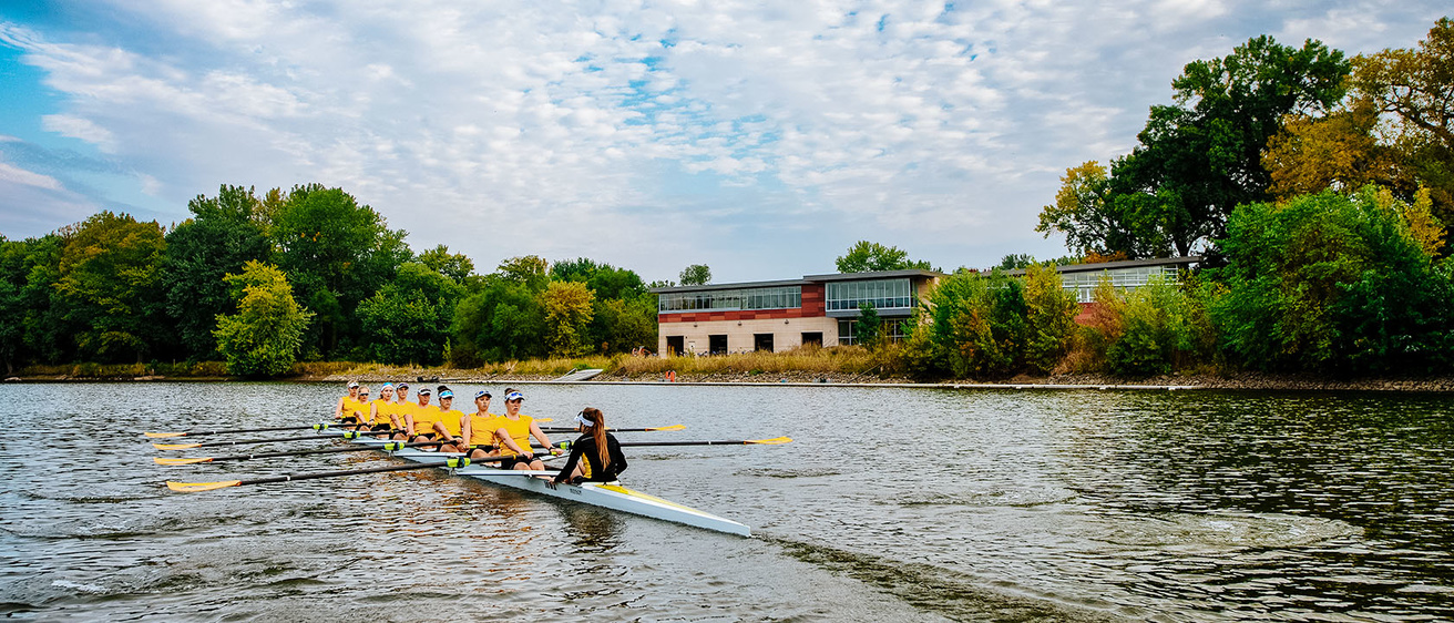 A rowing boat traverses the Iowa River in front of the boat house