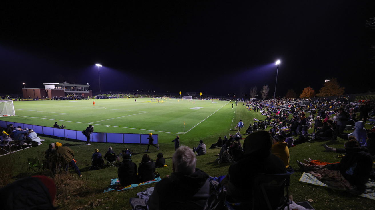 View of soccer field at night surrounded by fans.